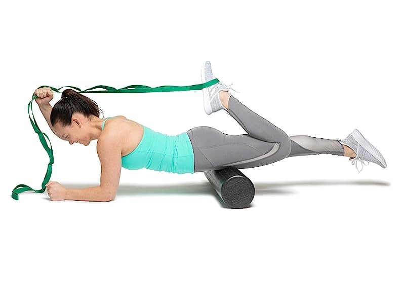 woman using stretch out strap on foot while balancing on foam roller